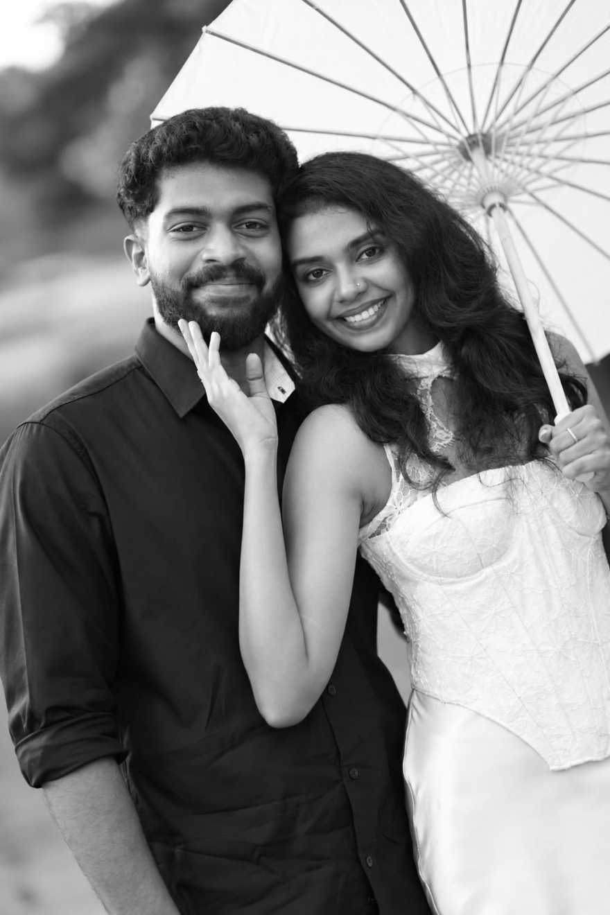 Abhijith and Aiswarya smiling together under a white parasol